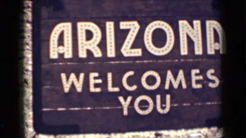 Arizona welcome sign fills the frame, with marquee-style white lettering against a dark wooden background on 8mm film.
