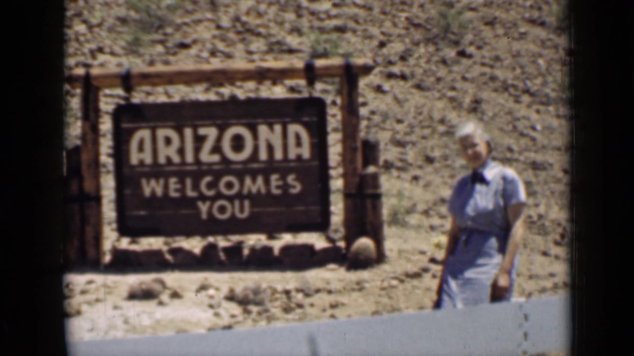 1939 Arizona roadside view with a rustic welcome sign and a woman posed at the edge of the frame.