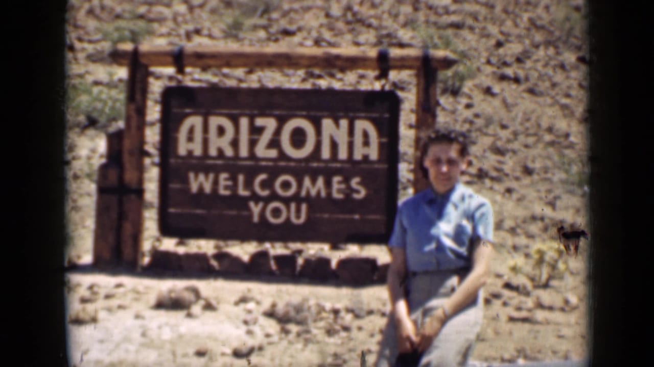 Woman posing beside a wooden sign reading Arizona welcomes you in rocky desert terrain.
