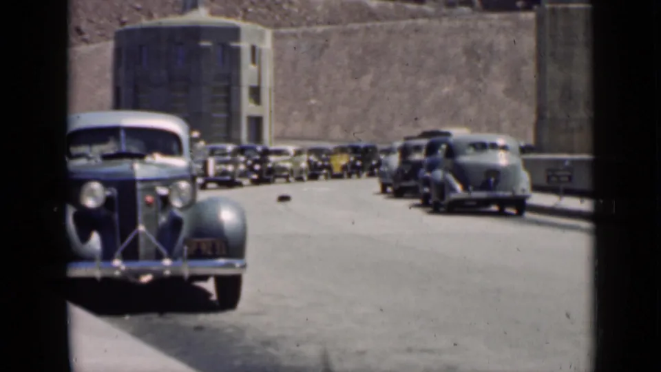 1939 Arizona home-movie view of vintage cars along a paved road near a large concrete dam-like structure and rocky desert wall.