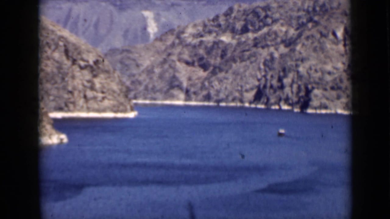 Small vessel on blue lake water below rocky canyon cliffs.