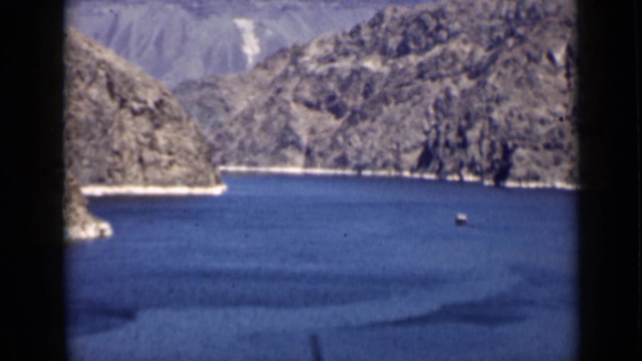 Blue lake and rocky cliffs with a small vessel near the right side.