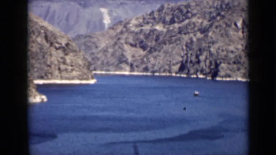 1939 Arizona 8mm view of blue lake water, a small vessel, and rugged cliffs along the shoreline.