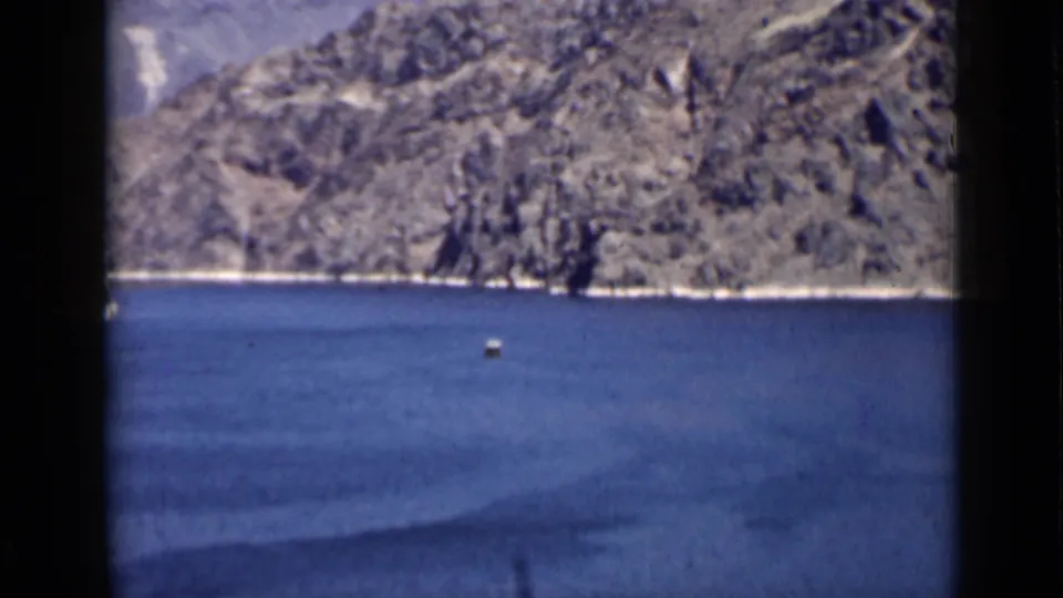 1939 Arizona travel footage frame showing a small vessel on blue lake water below rugged canyon cliffs.