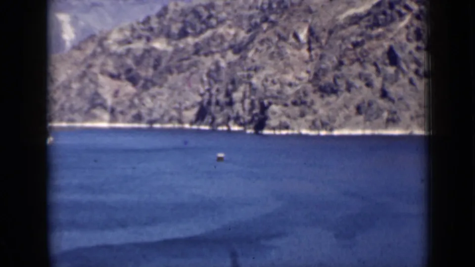 1939 Arizona home-movie frame showing blue lake water, rugged mountain slopes, and a small buoy in the distance.