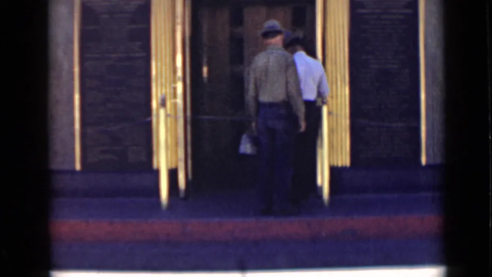 Two adults, one wearing a hat, enter a public-looking doorway in 1939 Arizona home-movie footage.
