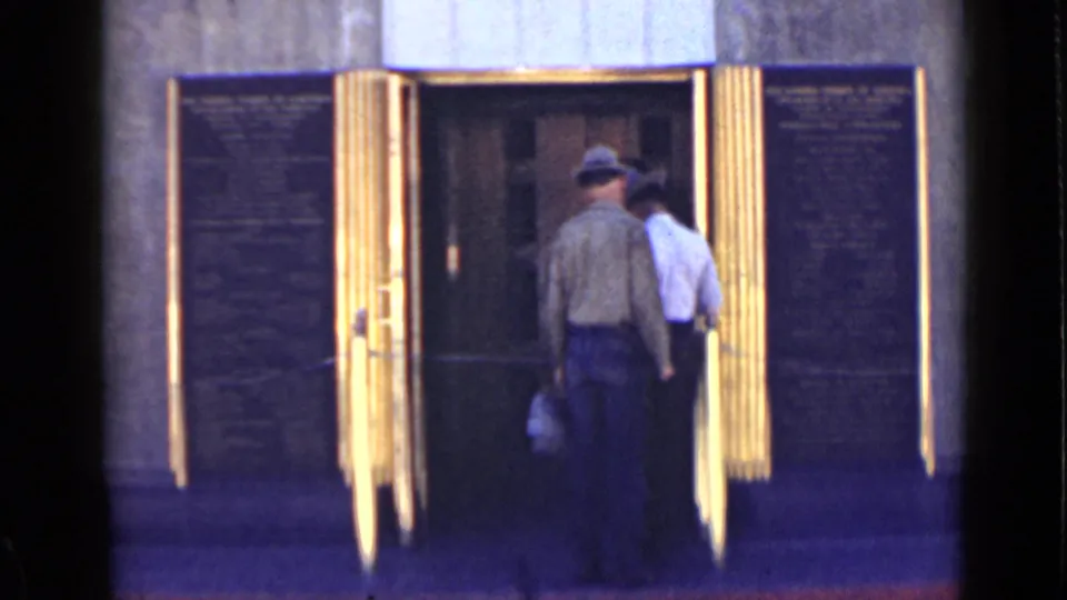 Two adults continue into a gold-toned entrance, seen in soft 8mm color from a visitor-shot perspective.