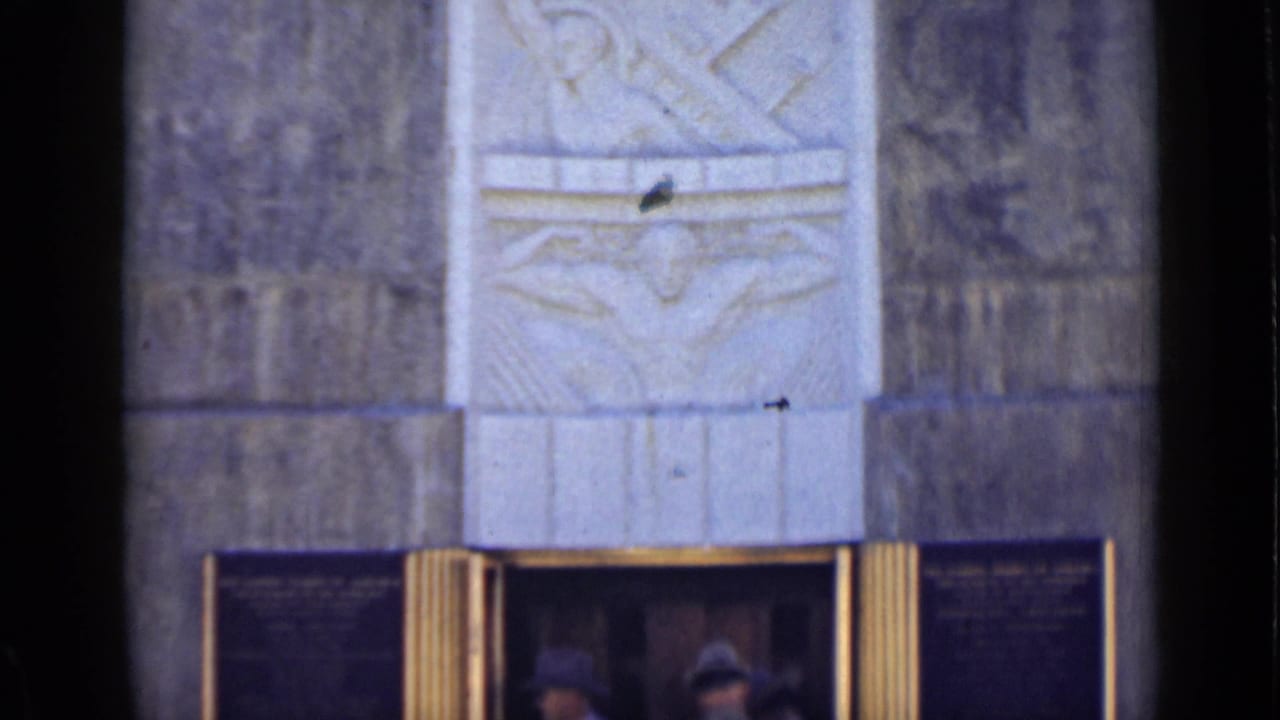 The camera frames the upper stone facade of the Arizona monument, showing carved relief work above the entrance.