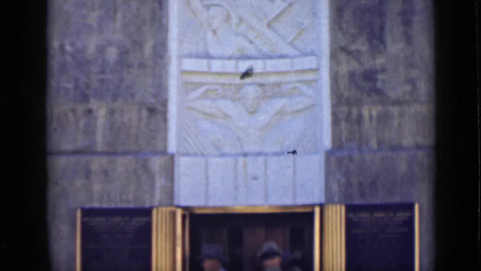 The camera frames the upper stone facade of the Arizona monument, showing carved relief work above the entrance.