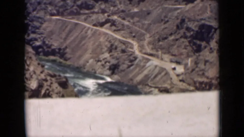A rugged Arizona canyon landscape appears from above, with a pale road tracing the slope and a river running below.