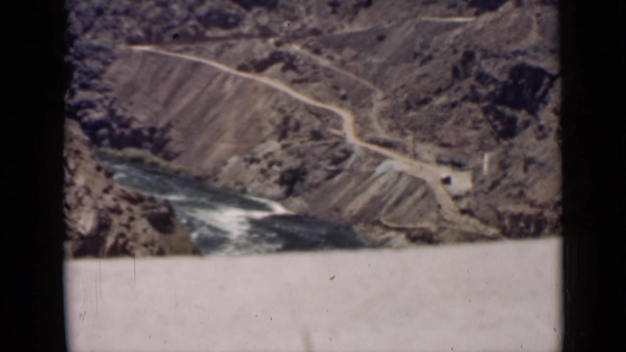 High view of a canyon road and river beside a dam structure.