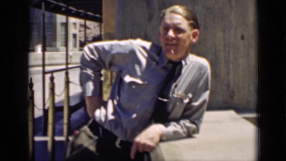 The officer remains beside the railing, partly seated or leaning, with concrete canal architecture behind him in the 1939 Arizona footage.