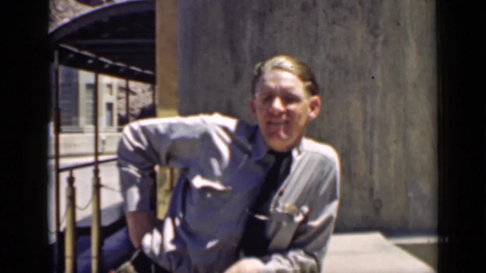 A light-uniformed officer with a visible face leans near the canal railing, with concrete walls and railings framing the Arizona home-movie shot.