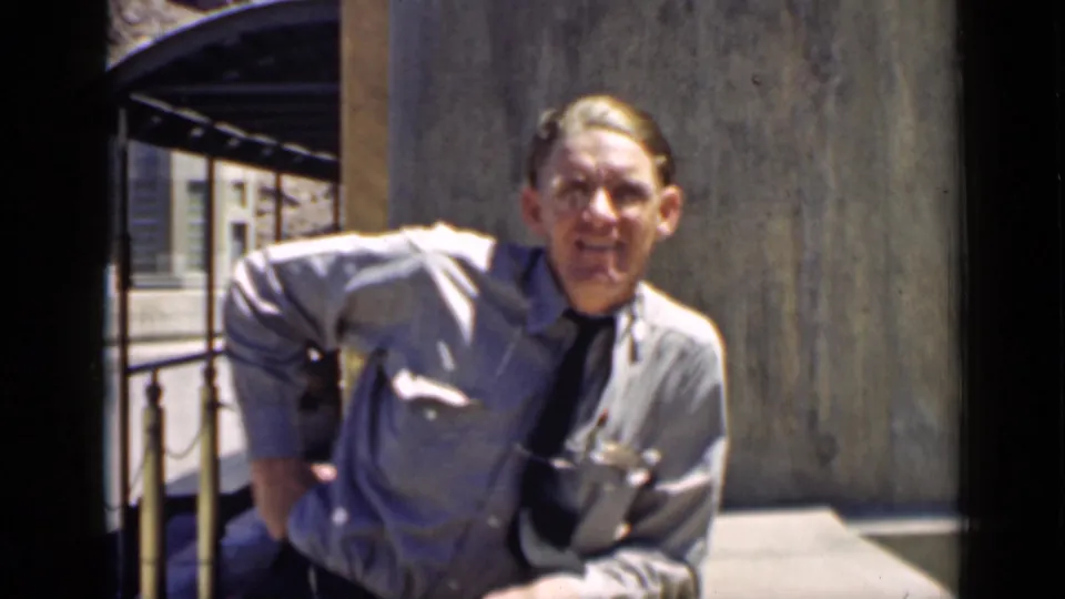 Adult man in 1939 Arizona home-movie footage smiles toward the camera while standing near a building exterior.