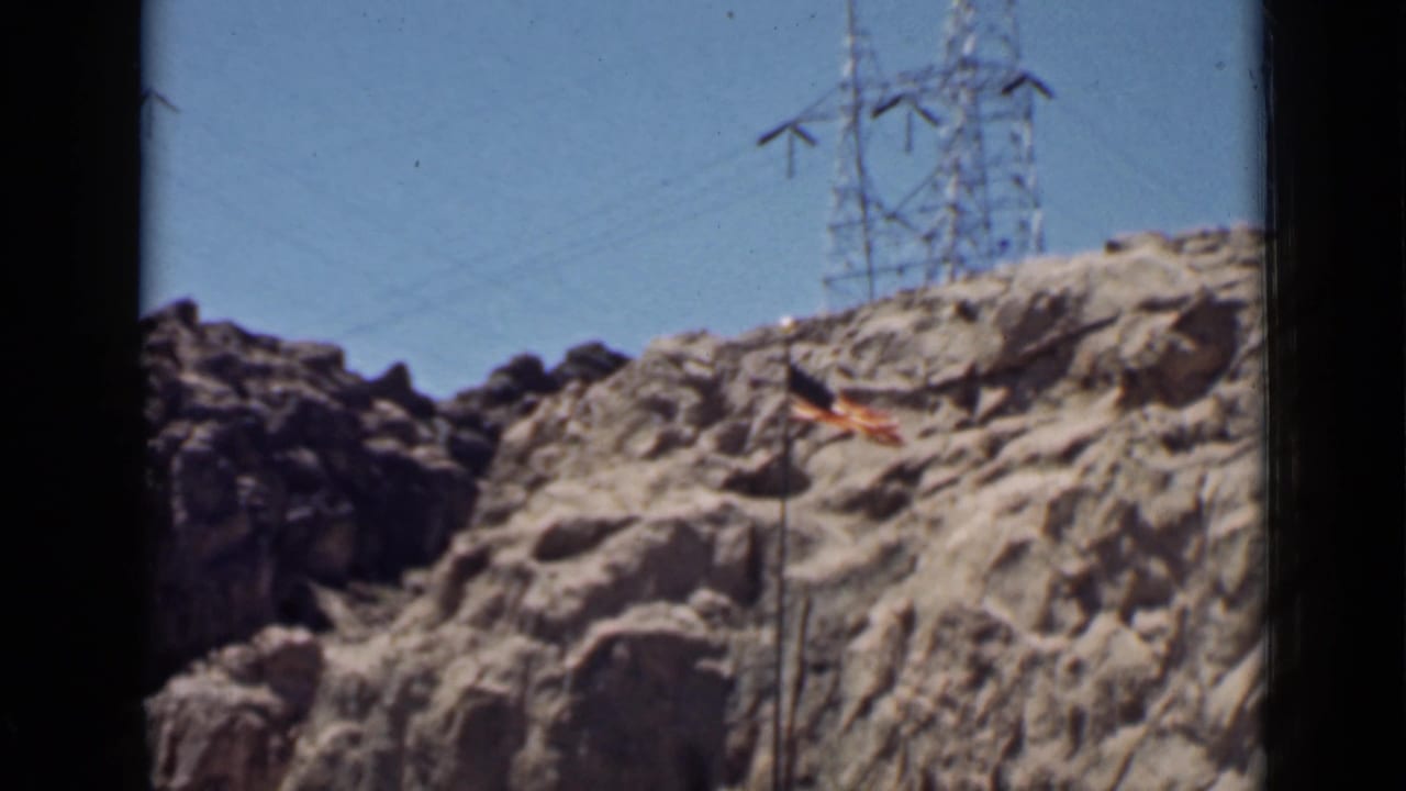 Rocky hillside with an American flag and power transmission tower under a clear sky.
