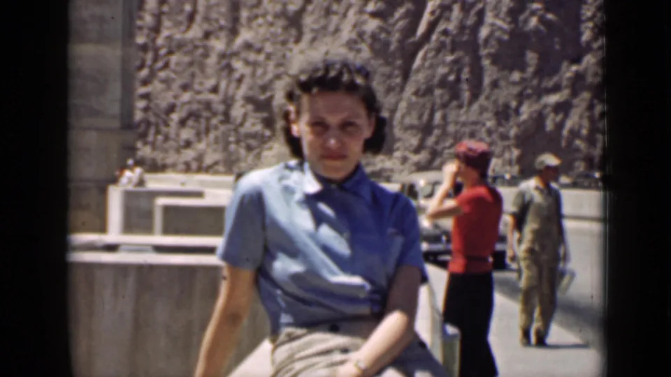 Arizona 1939 frame with the seated woman foregrounded, a woman in red and a uniformed-looking man near the road, and rock cliffs behind.
