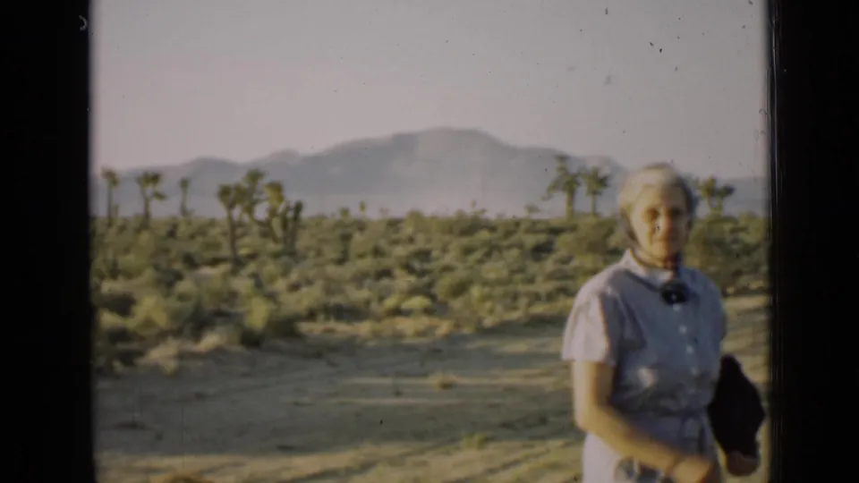Older woman poses in an Arizona desert setting with Joshua trees and distant mountains, filmed on 8mm in 1939.