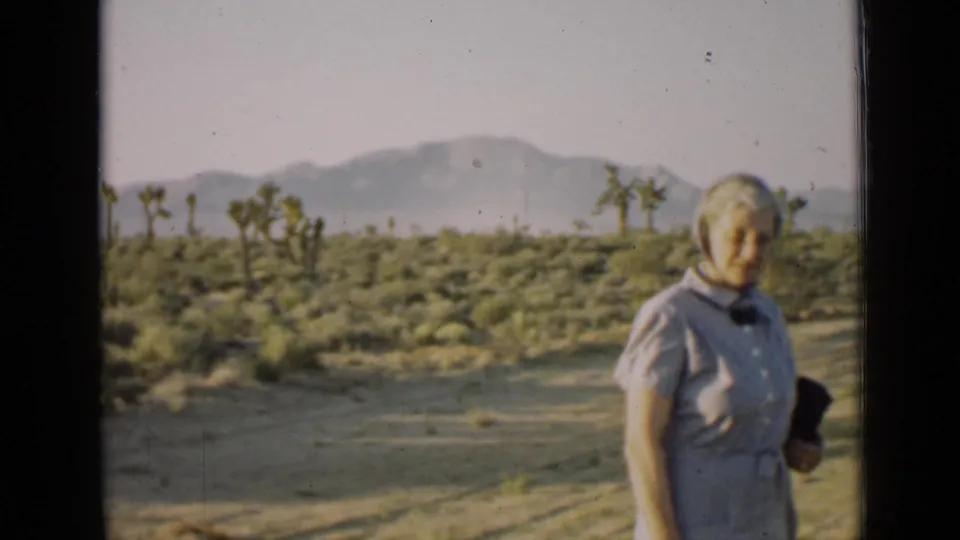 Older woman stands partly to the right of frame in a 1939 Arizona desert scene with Joshua trees and distant mountains.