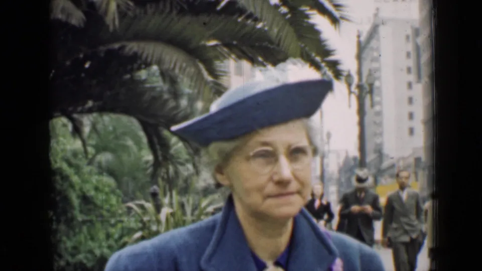 Older woman in formal blue clothing walks through an Arizona urban park in 1939 home-movie footage.