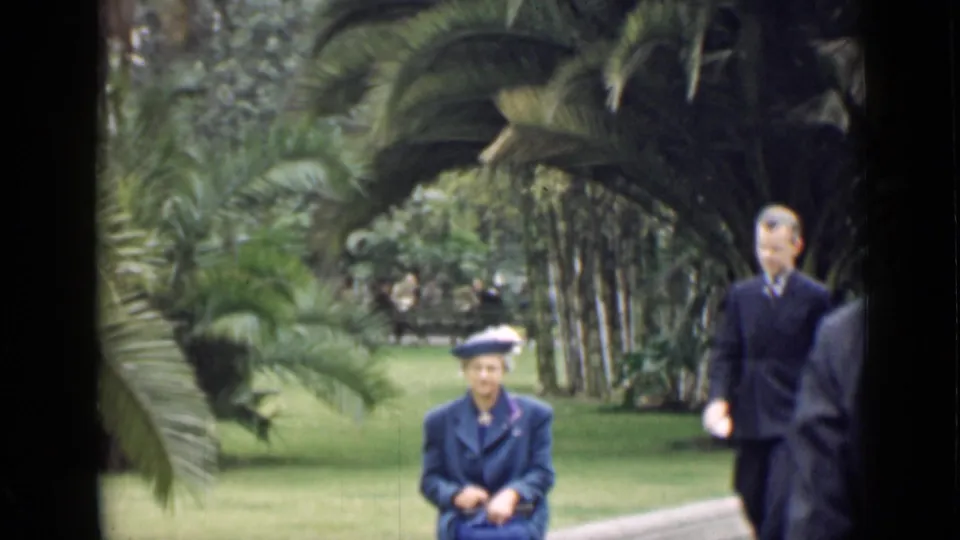 1939 Arizona garden frame with a seated woman on a ledge while a suited man passes near the right side.