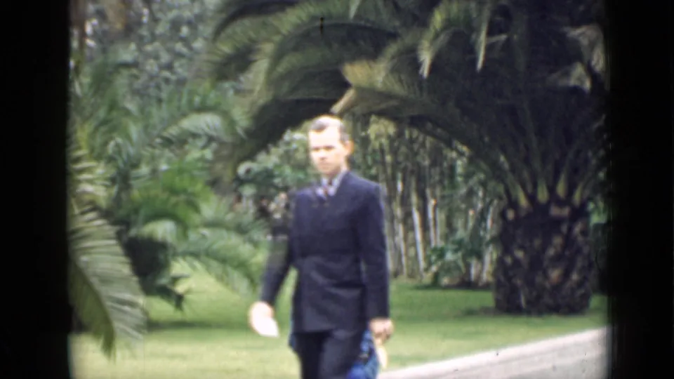 1939 Arizona 8mm frame of a man in a dark suit walking through a landscaped palm garden.