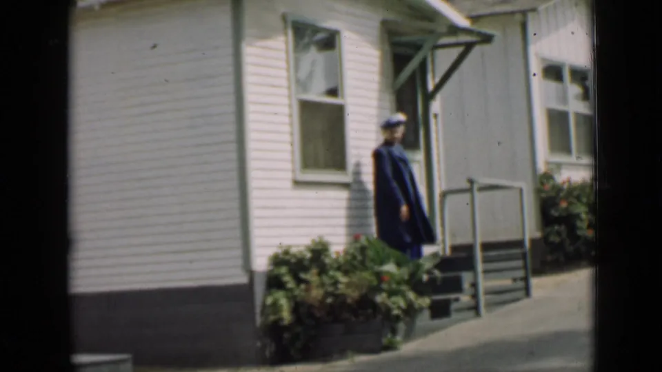 1939 Arizona frame with a uniformed adult in a dark coat and cap near porch steps on a white-sided building.