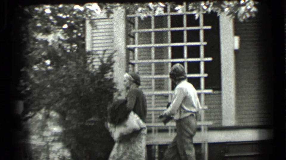 The women step from the porch area toward shrubs and trees, continuing the brief domestic exchange in Clear Lake home-movie footage.