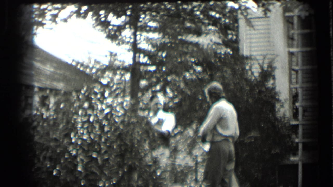 Two women continue through a shaded yard beside the Clear Lake house, partly obscured by shrubs and overhanging branches.