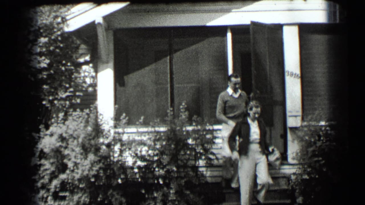 A man and woman stand at the front steps of a house with a screened porch.