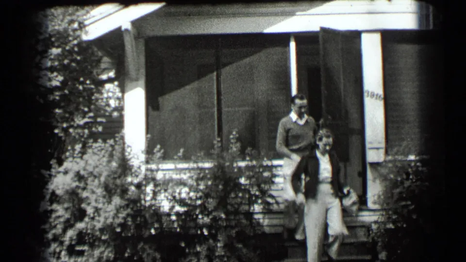 A man and woman appear on the front steps of a Clear Lake house, with porch screens, shrubs, and partial house numbers visible.