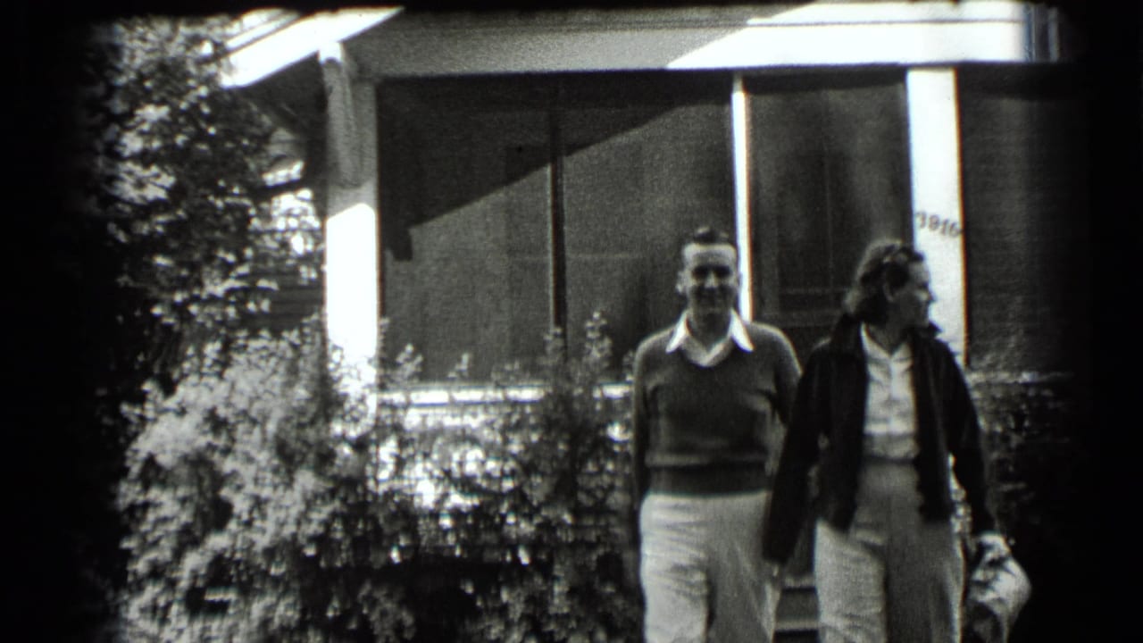 Man and woman walking outside a house with shrubs in front.