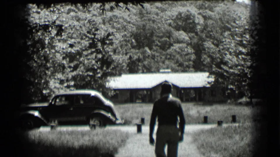 A man walks across a lawn toward a parked vintage car and low building in Clear Lake, California.
