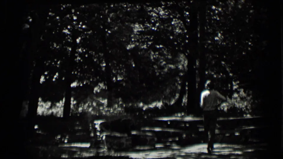 In 1939 Clear Lake home-movie footage, a man walks away through trees near picnic tables in a shaded outdoor area.