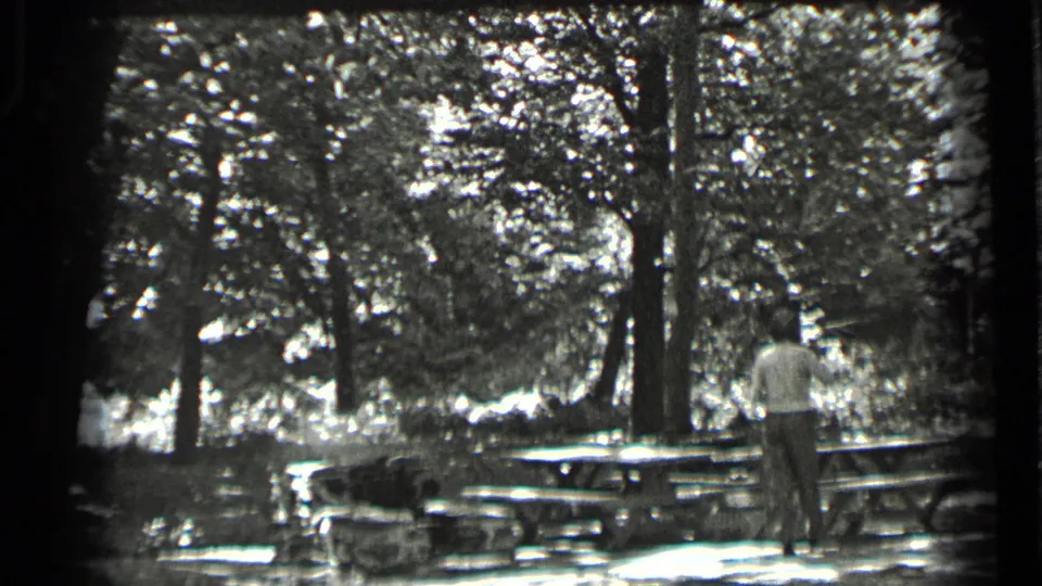 A man stands beside picnic tables under trees at Clear Lake, California, in dated 1939 black-and-white home-movie footage.