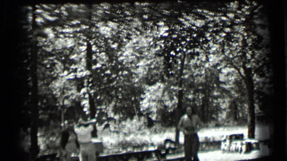 1939 Clear Lake frame showing several people in a wooded picnic area, with benches and dense foliage behind them.