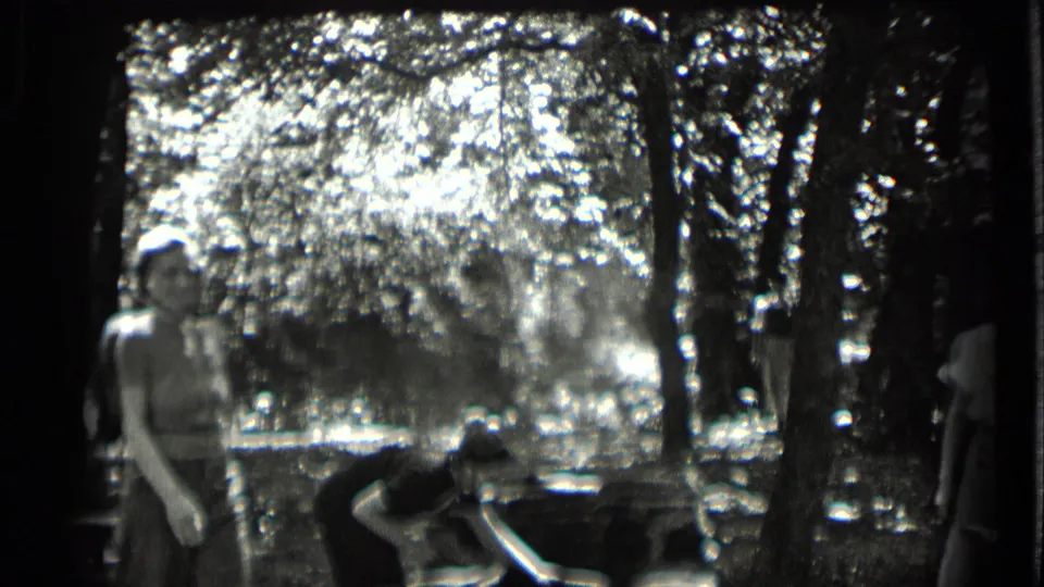 1939 Clear Lake home-movie frame showing young people around picnic tables in a shaded wooded area near reflective water.