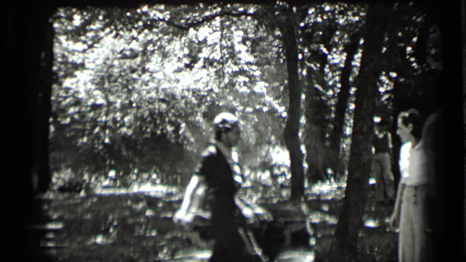 1939 Clear Lake home-movie frame showing two young women in a wooded picnic area beside reflective water.