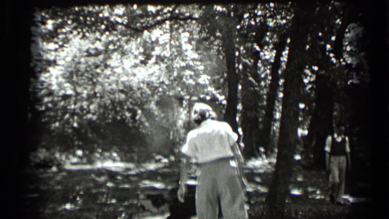 1939 Clear Lake home-movie frame showing adults in a wooded area, with one light-clothed figure walking away from the camera.