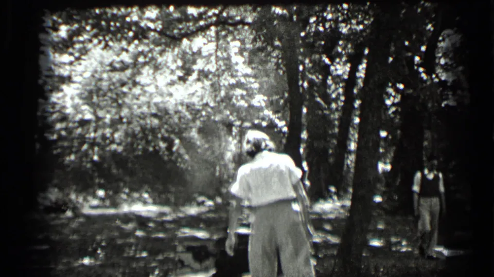 1939 Clear Lake home-movie frame showing adults in a wooded area, with one light-clothed figure walking away from the camera.
