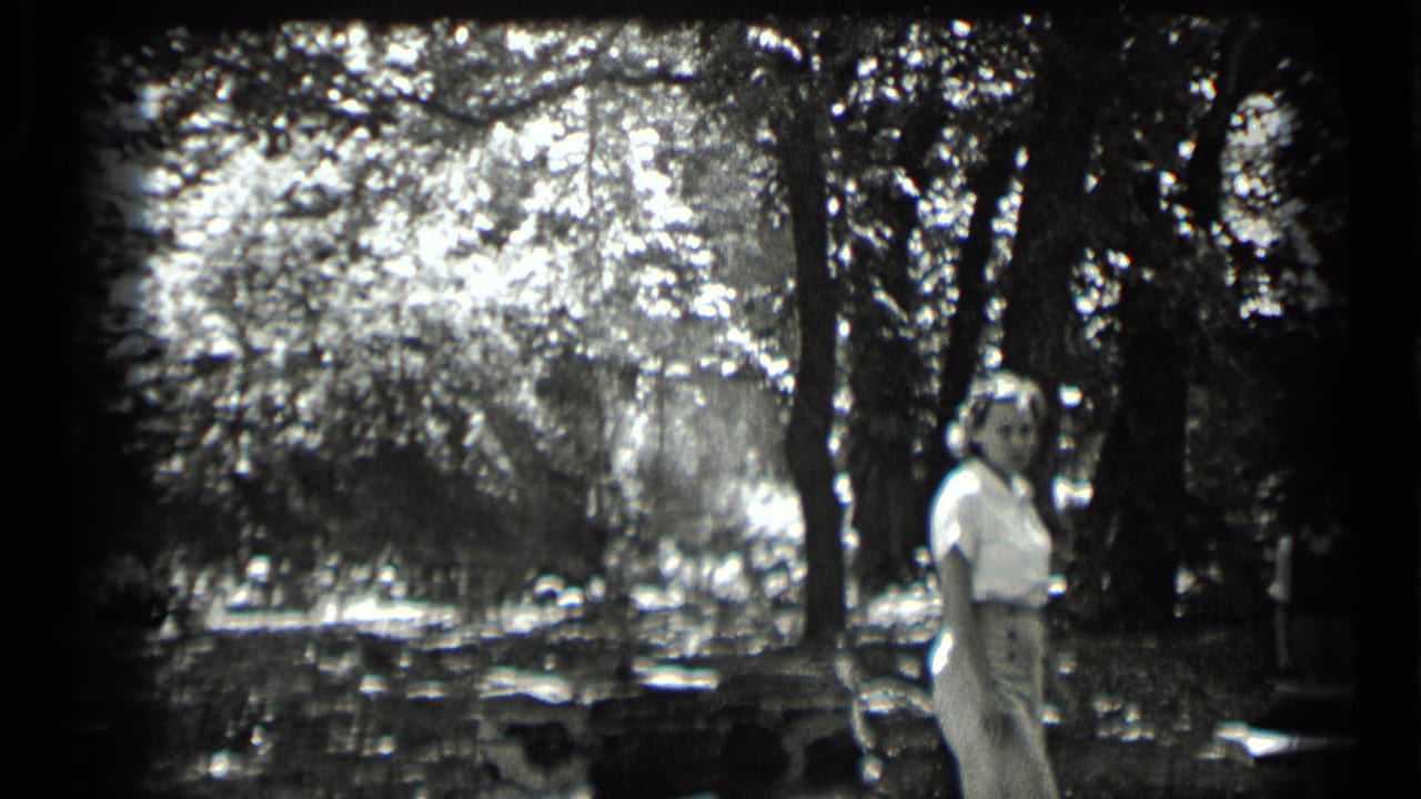 1939 Clear Lake frame with a woman in light clothing turning toward the camera beside trees and bright foliage.