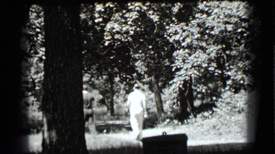 1939 Clear Lake home-movie frame showing two adults walking away through trees, one in light clothing and one darker dressed.