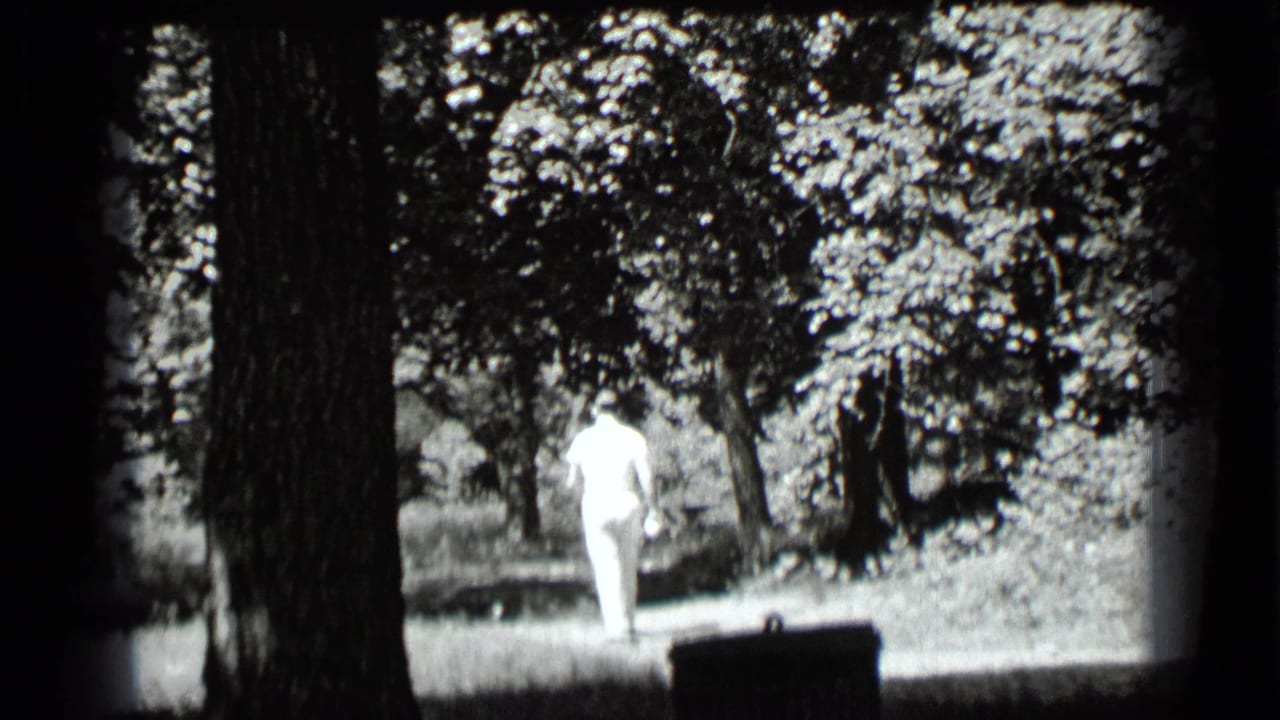 Man in light clothing walking away through a wooded area beside large trees.