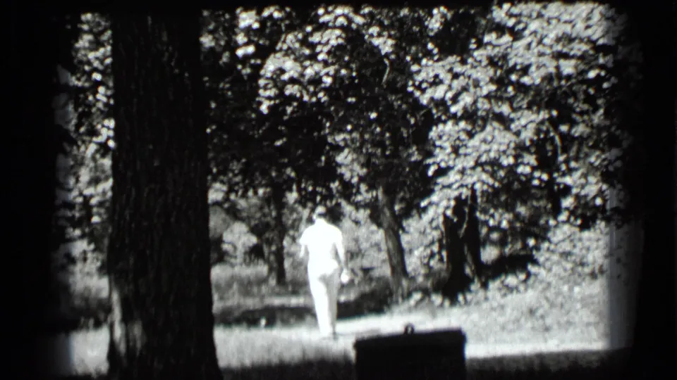 In 1939 Clear Lake home-movie footage, a man in light clothing walks through a shaded wooded area with large tree trunks nearby.