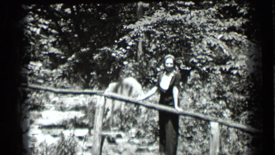 At Clear Lake, California in 1939, a woman in a dark dress and light head covering smiles near stone steps and a wooden railing.
