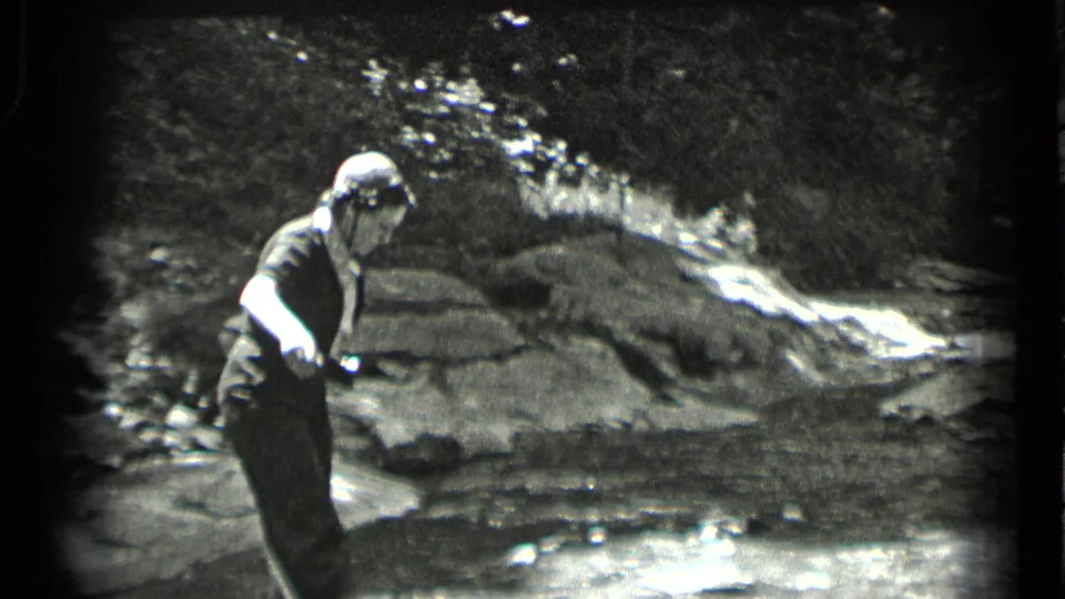 The woman stands near a small stream or rocky watercourse at Clear Lake, California, in grainy black-and-white 8mm footage.