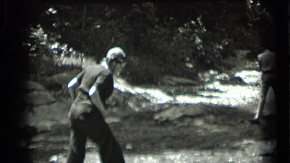 1939 Clear Lake footage shows a woman near the waterline with another adult partly visible on the rocky bank.