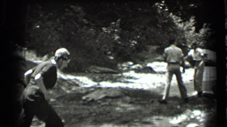 A 1939 Clear Lake home-movie frame shows a woman in the foreground and two adults examining the rocky stream area.