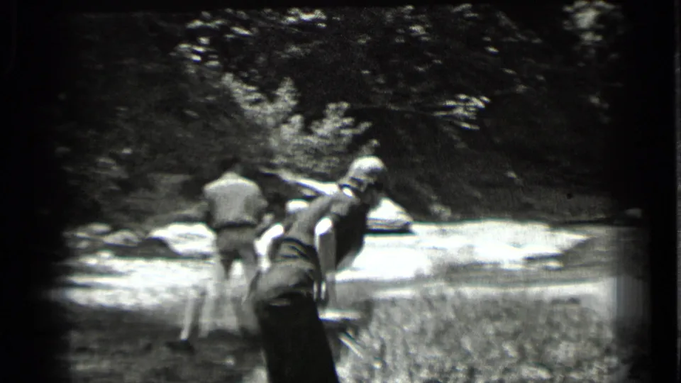 1939 Clear Lake footage shows a woman leaning at the water's edge with another adult standing farther along the rocky streambank.