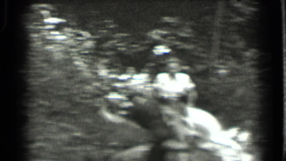 Soft 1939 8mm frame from Clear Lake showing a woman in light clothing carefully moving through a shallow wooded stream.