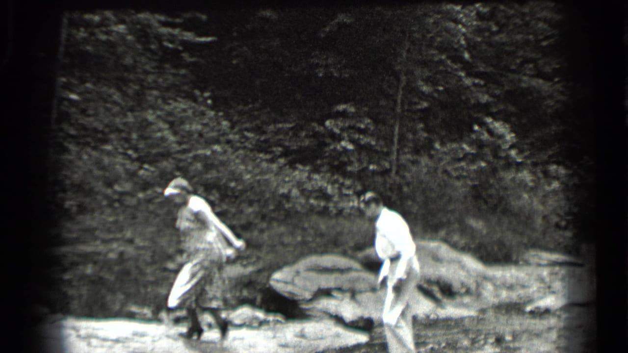Woman steps over the creek while a man follows across the rocky bank.